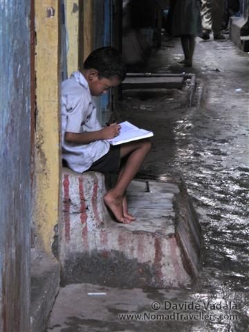 On the residantial sector a kid is trying to do his homework on the steps of his house, probably for the absence of light inside. The slum are so crowded that there is no space for windows and light. Often also the roads are really narrow, and the light is barely reaching the ground. 047 Mumbai-Bombay-Dharavi-Slum India 3931